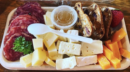 A charcuterie box with three different kinds of cheese, crackers, salami, jam, and strawberries